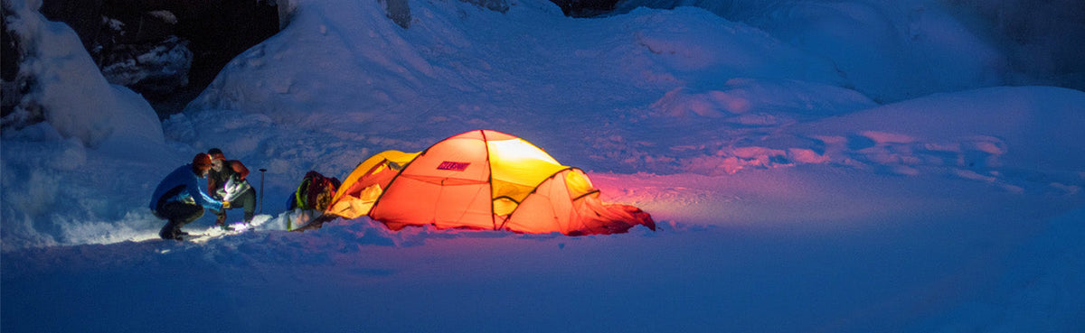 Drei Personen bauen bei Schneefall ein Zelt auf